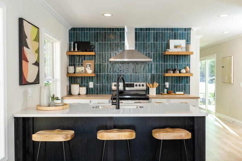 Manufactured kitchen with white walls, an accent wall with vertical, teal tile, and a large breakfast island directly across from it.