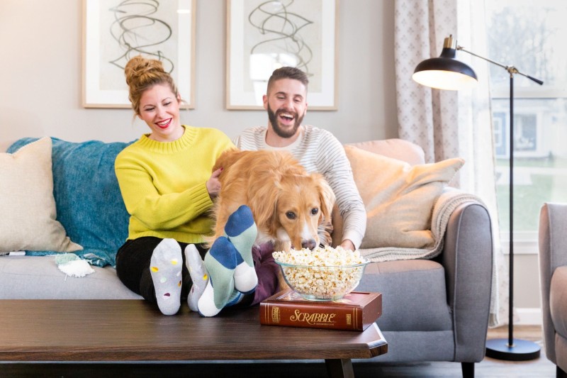 A couple sitting on the couch with their dog in a manufactured home living room eating popcorn.
