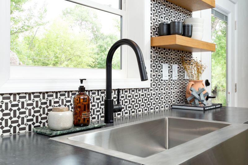 Stainless steel sink with window behind it and black and white patterned tile as backsplash.