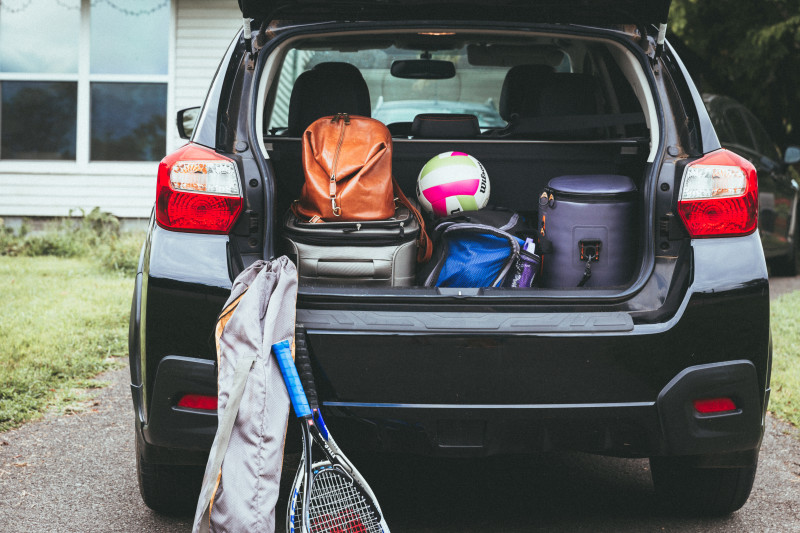 The trunk of a small, black crossover is open with luggage and sport equipment packed in the back.