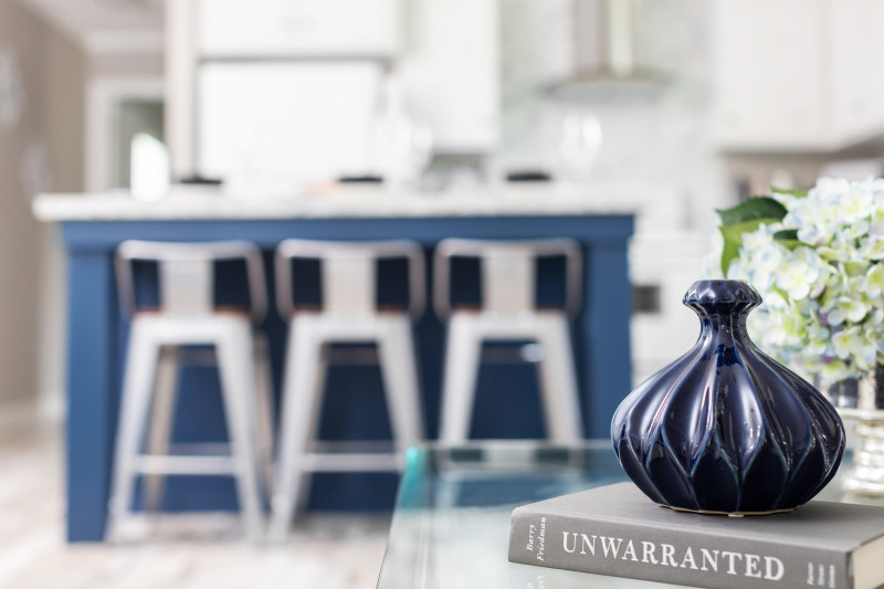 Picture of a blue vase with a blue kitchen island with white chairs in the background.