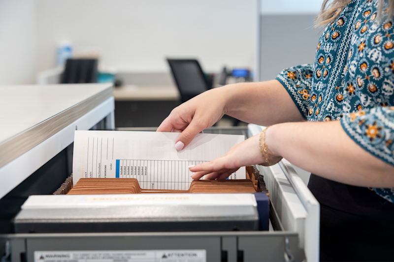A close-up of hands sliding a document in a file in an open cabinet.
