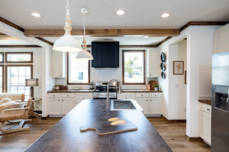 Kitchen of a Clayton manufactured home with a large island, stove and range hood in a wall with windows, ceiling beam and pendant lights