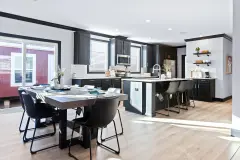 View of the dining area and kitchen in the Louis home model from Clayton, showing a table set for six, a kitchen island with three bar stools, a coffee bar, and black cabinetry.