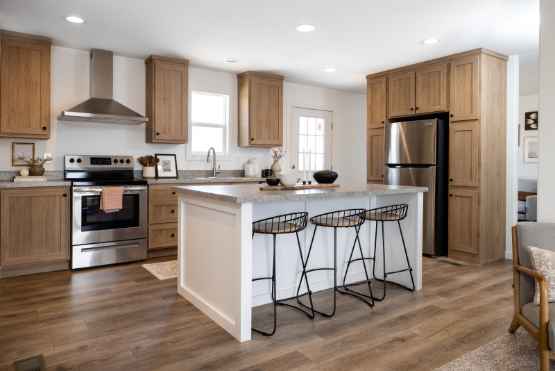 Kitchen of a Clayton home with light wood cabinets and floors, white island with stools, white walls and stainless steel appliances