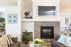  There's a living room in view with a stack stone fireplace with a tv above it and furniture across from it. The area is decorated with plants. 