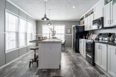 A gray kitchen in a manufactured home with white cabinetry and gray wall panels with batten strips.