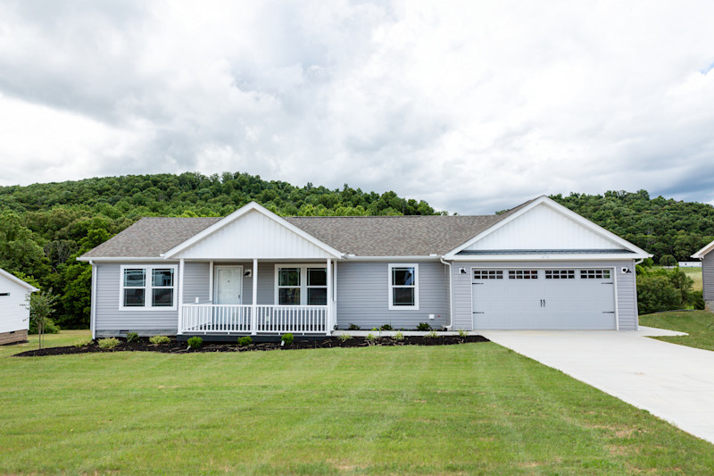 CrossMod home with gray siding and roof, white trim on the porch, attached garage and driveway and green lawn in front.