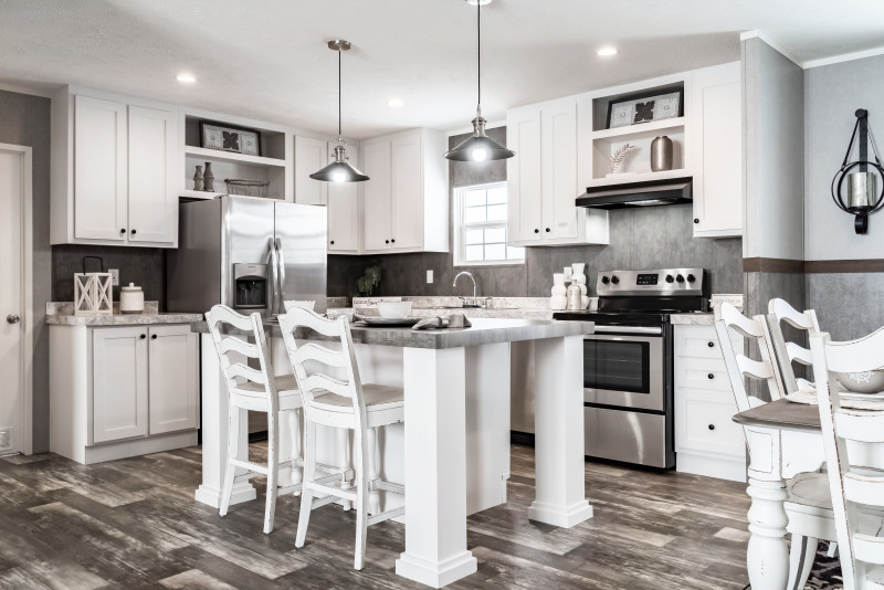 This kitchen is bright white, with a eat-at kitchen island, stainless steel appliances, and modern black lighting sconces hanging down over the island.