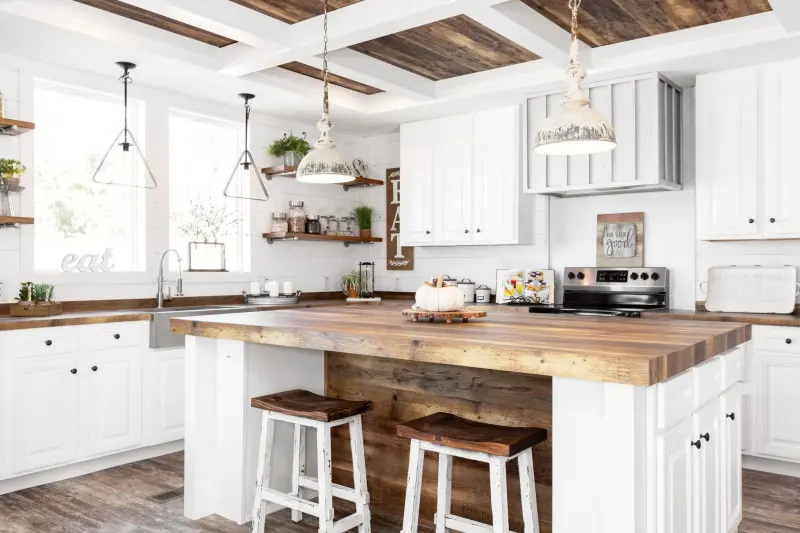 Farmhouse kitchen in a Clayton manufactured home, with white cabinets, butcher block style countertops, white walls, weathered flooring and farmhouse decor.