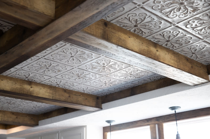 Brown wooden ceiling beams with light brown and white metal tiles underneath.