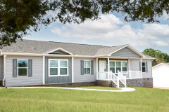 An exterior of a manufactured home with gray and green siding and a front porch.