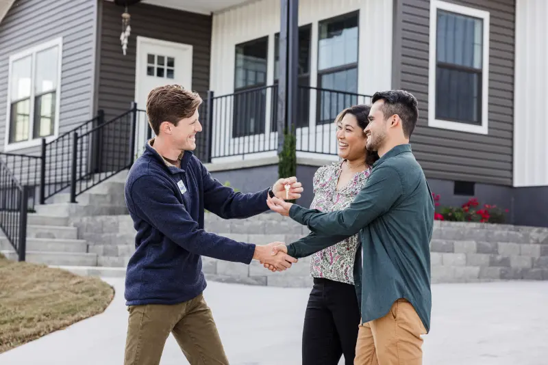 A couple shakes hands with a home center sales consultant while being handed the key to their new house.