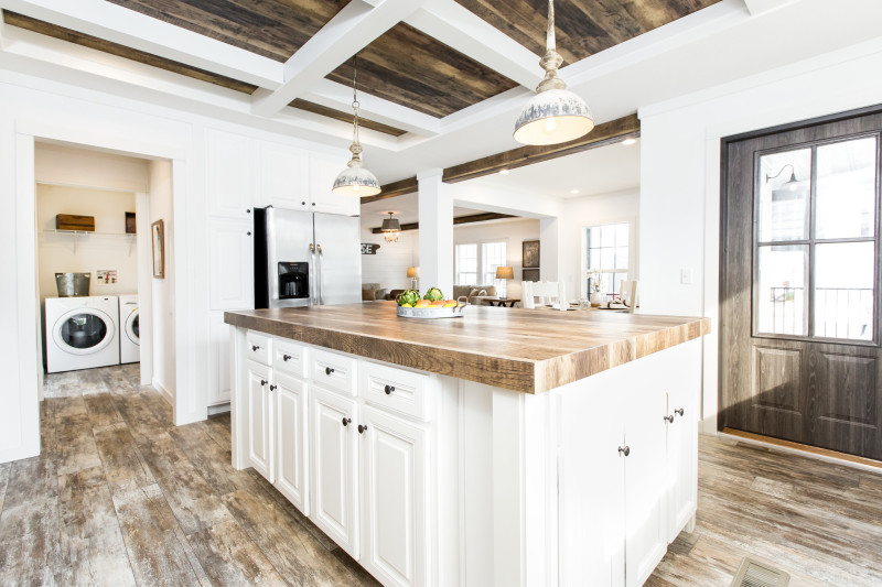 A manufactured home kitchen with an island, hanging lights, washer and dryer and vinyl flooring