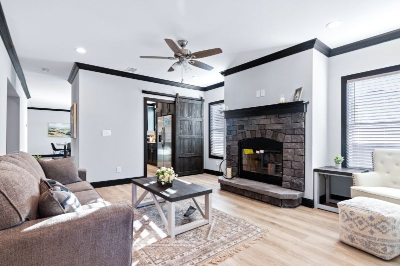 View of the family room inside the Louis home model from Clayton, showing a couch and coffee table in front of a gray stone fireplace and a barn door that connects to the butler’s pantry and kitchen.