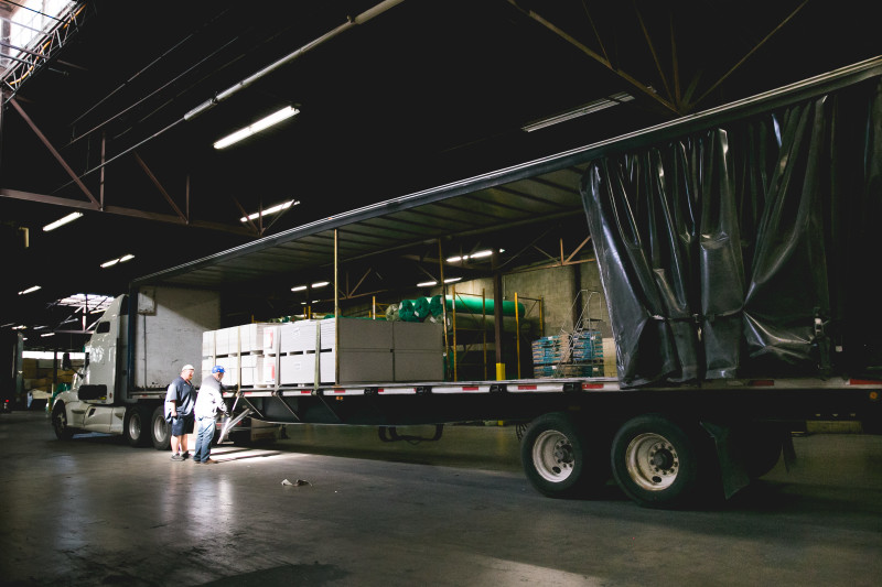 Two men unloading a truck full of materials in a manufactured home building facility.