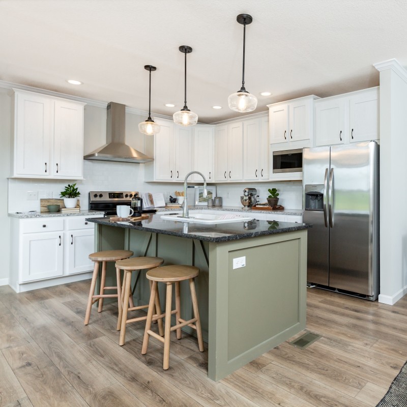 Kitchen features white cabinets, a sage kitchen island with a black top and sink in it. There are stainless steel appliances as well the kitchen hood. Plus, there are 3 wooden stools pulled up the island.
