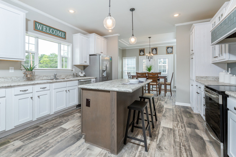 Kitchen of a Clayton home featuring weathered style flooring, white cabinets, marble style counters and a medium wood island, with stainless steel appliances, with a doorway leading to the dining room in the background.