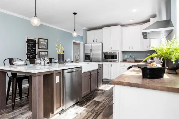 The [model name] has this gorgeous kitchen featuring a huge island with seating and a built-in sink, along with tall white cabinets for plenty of storage and an attached dining room.
