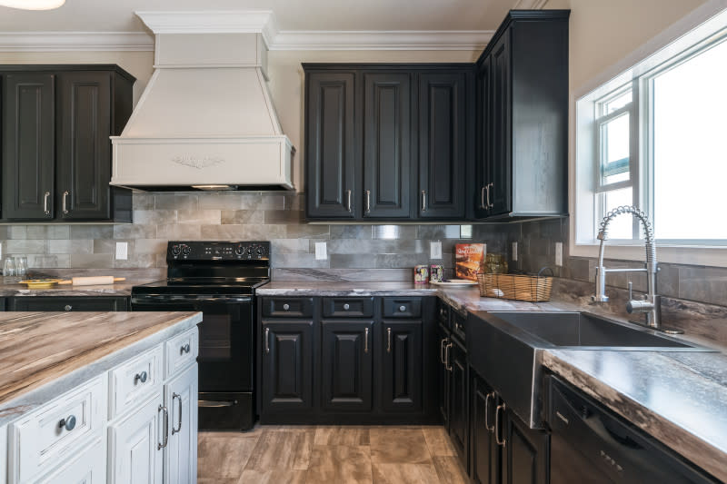 : A kitchen in a manufactured home with black cabinets, a kitchen island and farmhouse sink.