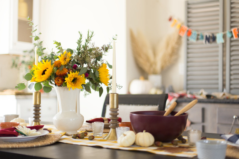 Sunflower filled vase sitting in the center of a Thanksgiving table.