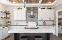 A farmhouse style kitchen in a manufactured home featuring a shiplap walls, island, white cabinets, coffered wood ceiling and steel range hood.