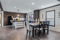 There’s a kitchen and dining area in a manufactured home. The kitchen has brown cabinetry, a white island and a table is set up in the dining area. 