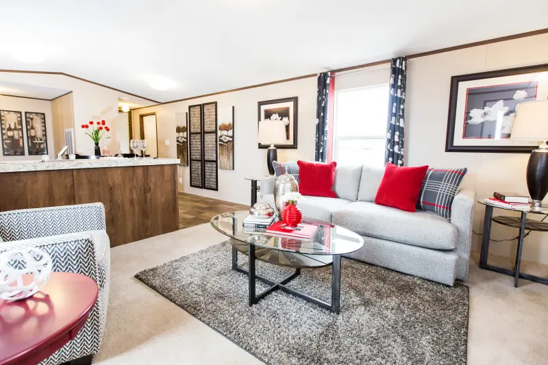 A living room leading into the kitchen with gray furniture and red accents in the pillows, art and coffee table décor.