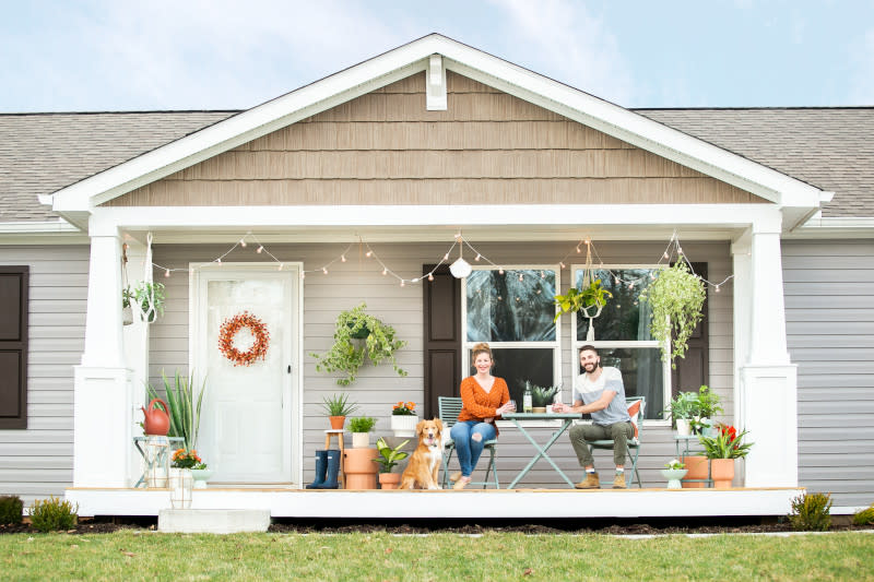 A young couple and their dog sitting on the decorated front porch of their manufactured home. 