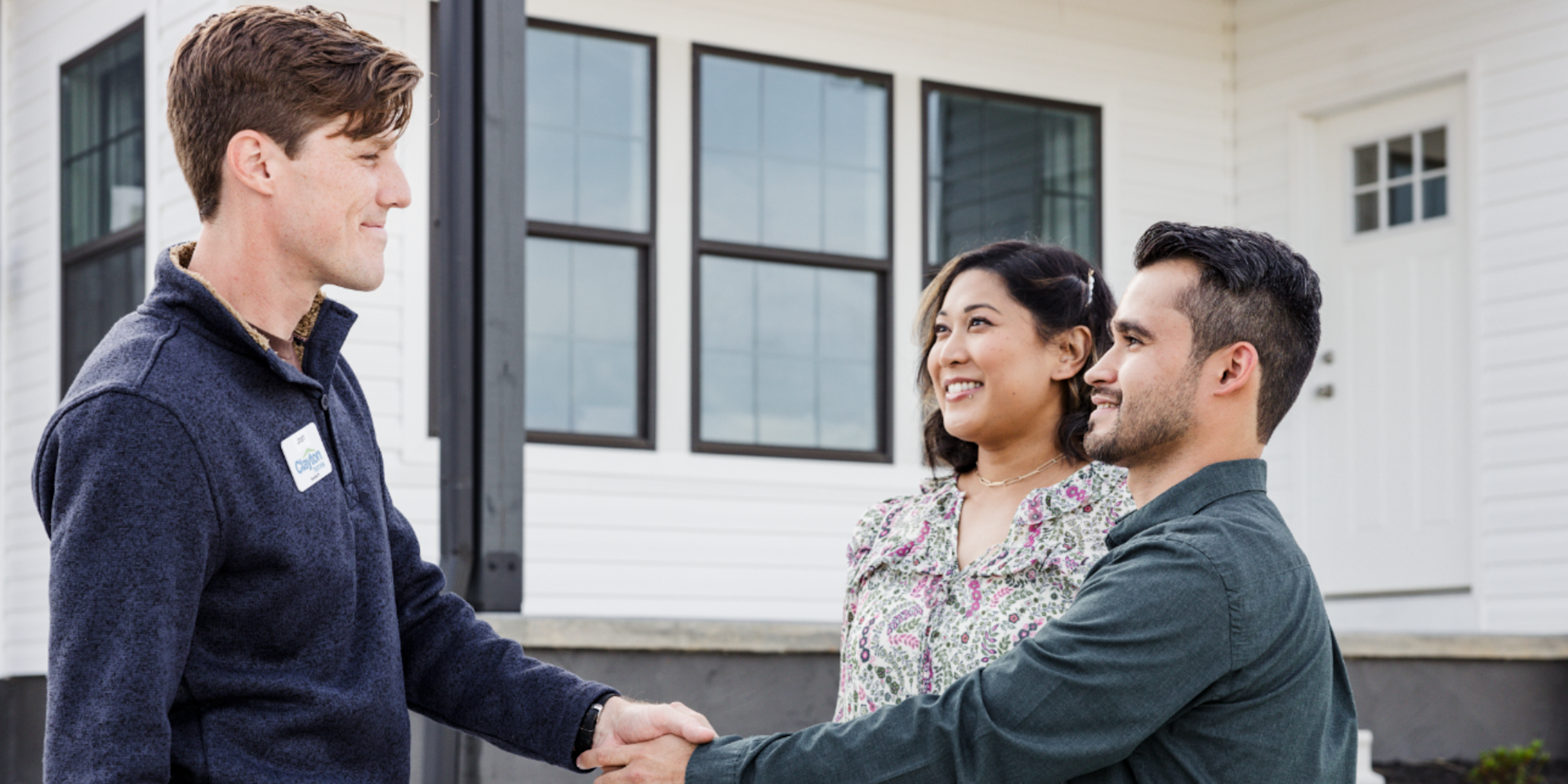 A couple shakes hands with a Clayton home center consultant in front of a white-sided home.