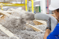 A worker sprays insulation into the roof of a manufactured home inside a home building facility. 