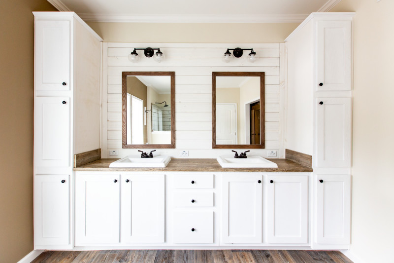 Manufactured bathroom with crisp white and wooden double vanity. Cabinets also encapsulate the vanity area.