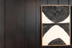 A close-up of a black wall with a framed abstract black and white painting hanging on it.