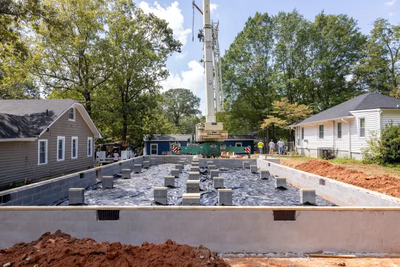 Pier and beam foundation prepared for a CrossMod manufactured home, with two houses on either side and a crane in the background