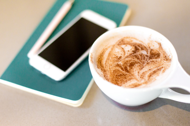 There is a coffee mug in view with a blue notebook, phone, and pen in the background.
