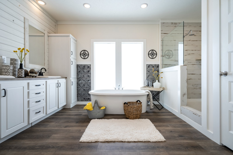 There’s a free-standing bathtub in view with windows behind it. To the right there is a walk-in shower, and to the left is a double vanity and cabinets for storage.