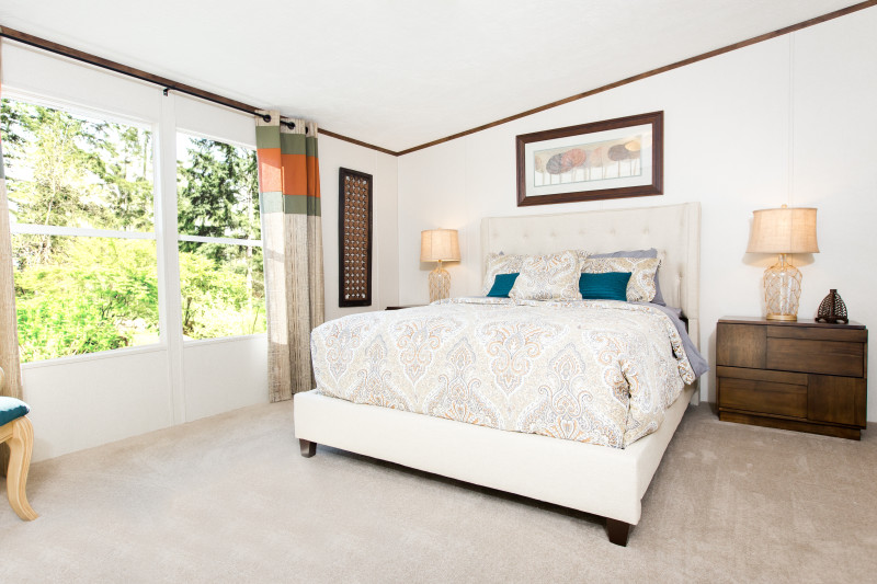 Manufactured home bedroom with large white bed in the middle of the room and window feature.