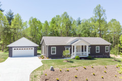 Manufactured home with dark brown siding, gray roof and white porch and trim, with a matching garage at the end of the driveway and a lawn in front of it.
