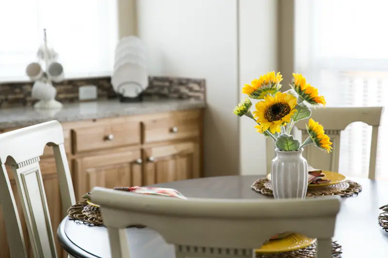 Wooden table with white chairs and a vase with sunflowers in it.