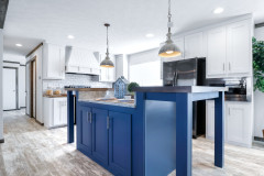 A blue kitchen island with pendant lights hanging over it is in the center of a kitchen with white cabinets and backsplash. 