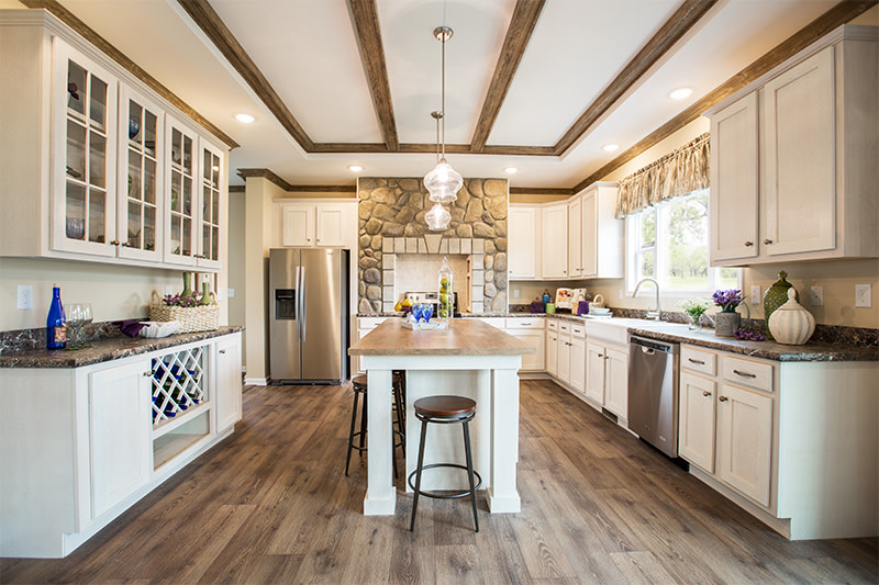 The 2483 Heritage kitchen has white cabinets, a kitchen island, ceiling beams and a stone range hood.