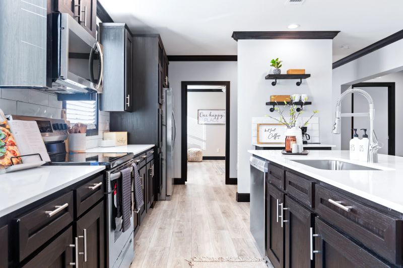 The kitchen of Clayton Homes' Louis home model if standing between the kitchen island and the opposite kitchen counter. There are stainless appliances, a coffee bar, white countertops, and black cabinets.