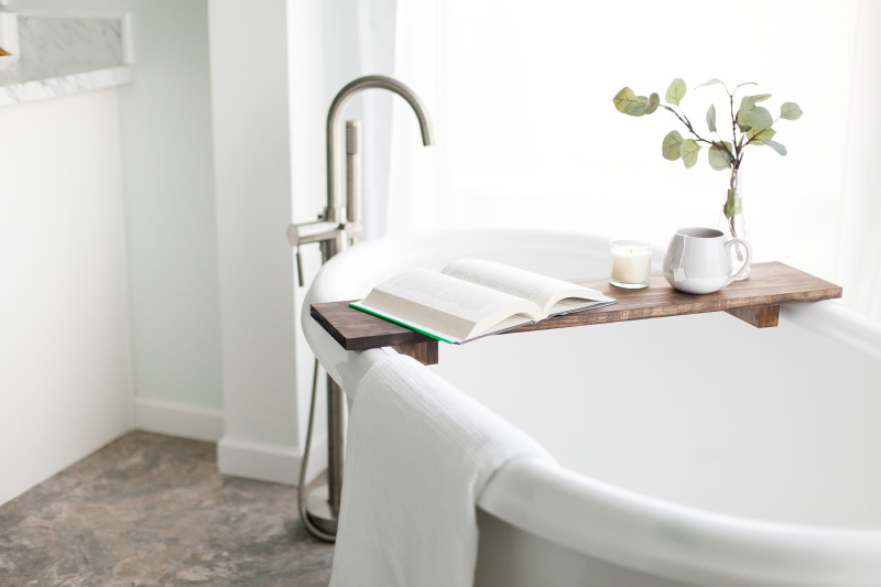 A relaxing soaking tub with a book and hot tea sitting on a tray.