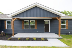 Exterior of a CrossMod home with dark blue siding, wood trim and a front porch with sidewalk.