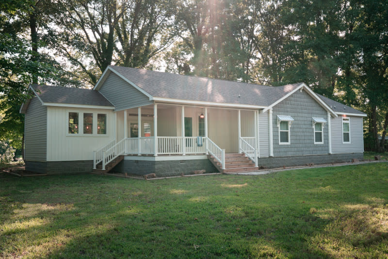 The Laney manufactured home model with white and gray siding, a large front porch, lawn and trees behind it.