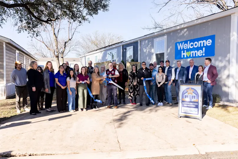 A group of people cut a large ribbon in front of a modern manufactured home