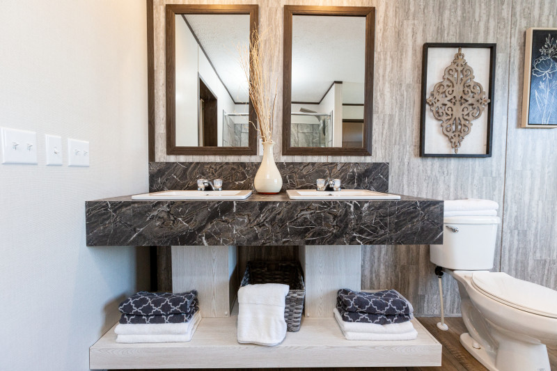Bathroom of a manufacture home featuring patterned accent wall and a double vanity with a bench.