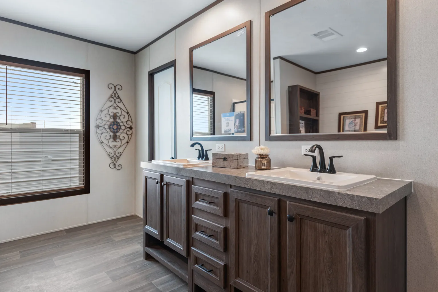 Tan bathroom with a brown double vanity with two mirrors above it.