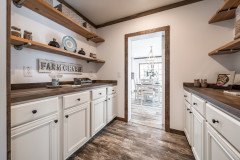  The inside of a farmhouse pantry with long, open shelving and white cabinets with wood-style counters on both walls.