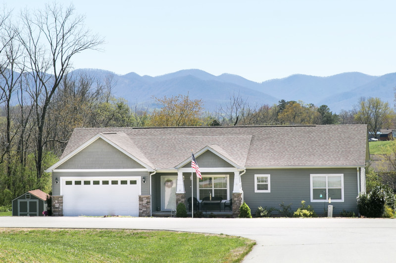 Exterior of a manufactured home with a garage and mountains in the background.